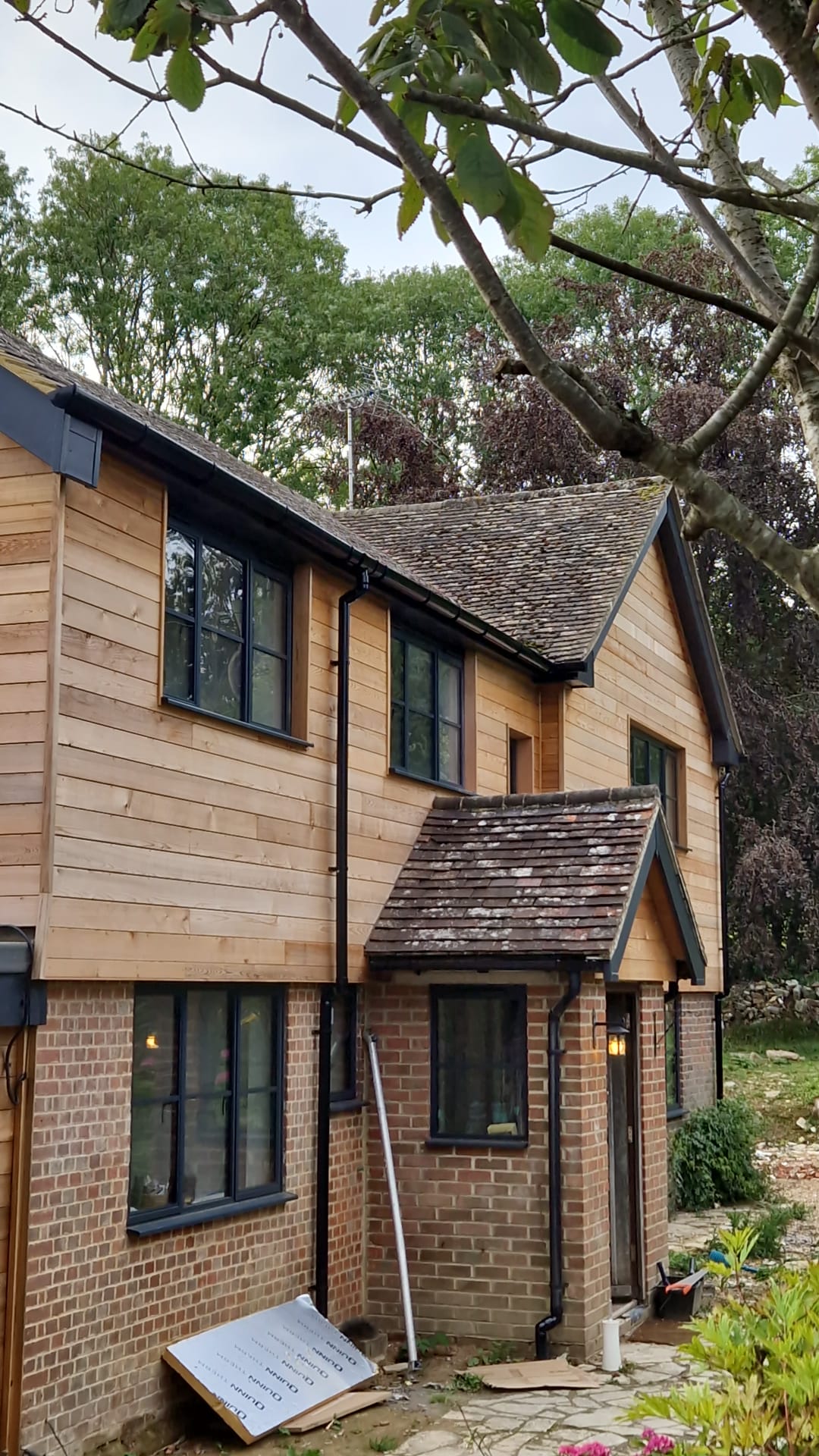 1960s house re-clad in natural cedar with black aluminium windows and new guttering by Two Build in East Sussex