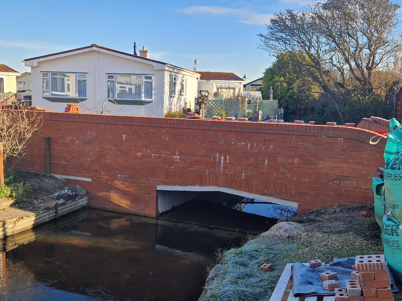 Bespoke red brick arch bridge built over a private waterway in East Sussex by Two Build, with curved parapet walls and coping