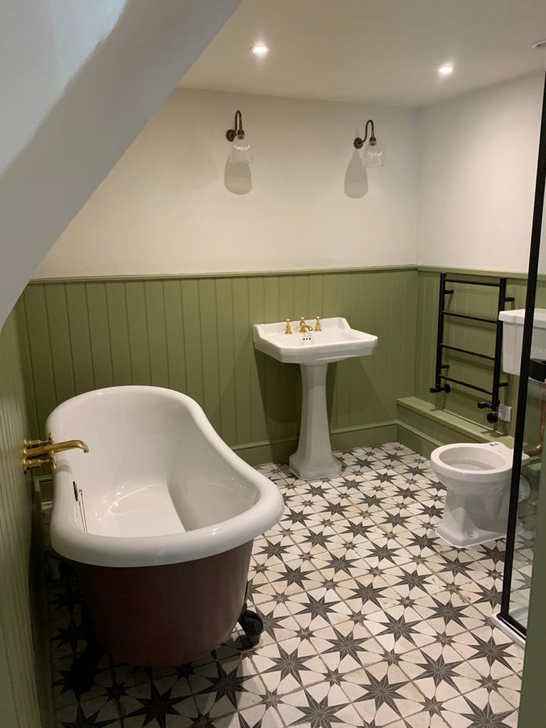Restored cottage bathroom with cast iron roll top bath, green tongue and groove panelling and patterned star floor tiles