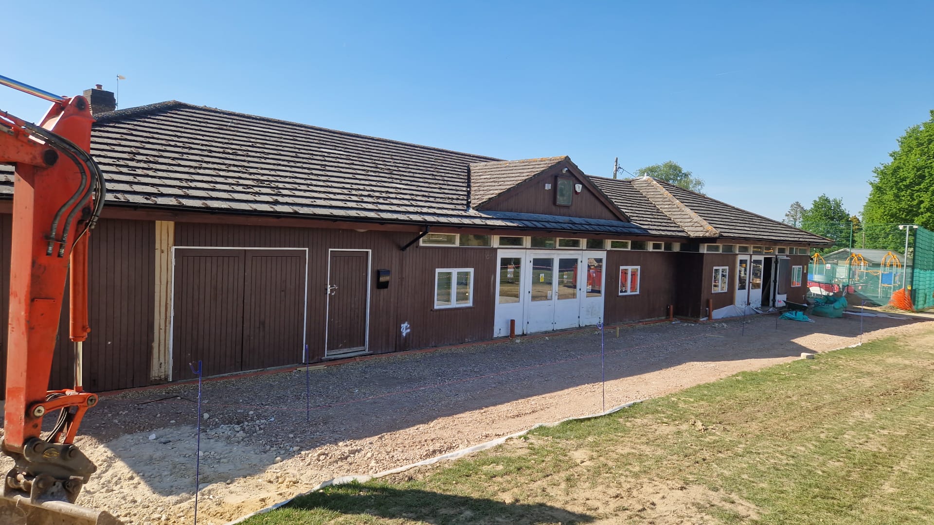 Sports clubhouse before renovation, showing dated dark brown timber cladding and groundworks underway on site