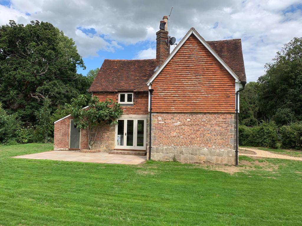 Rear elevation of a restored period cottage showing repaired brickwork, sandstone plinth and new French doors onto a stone patio