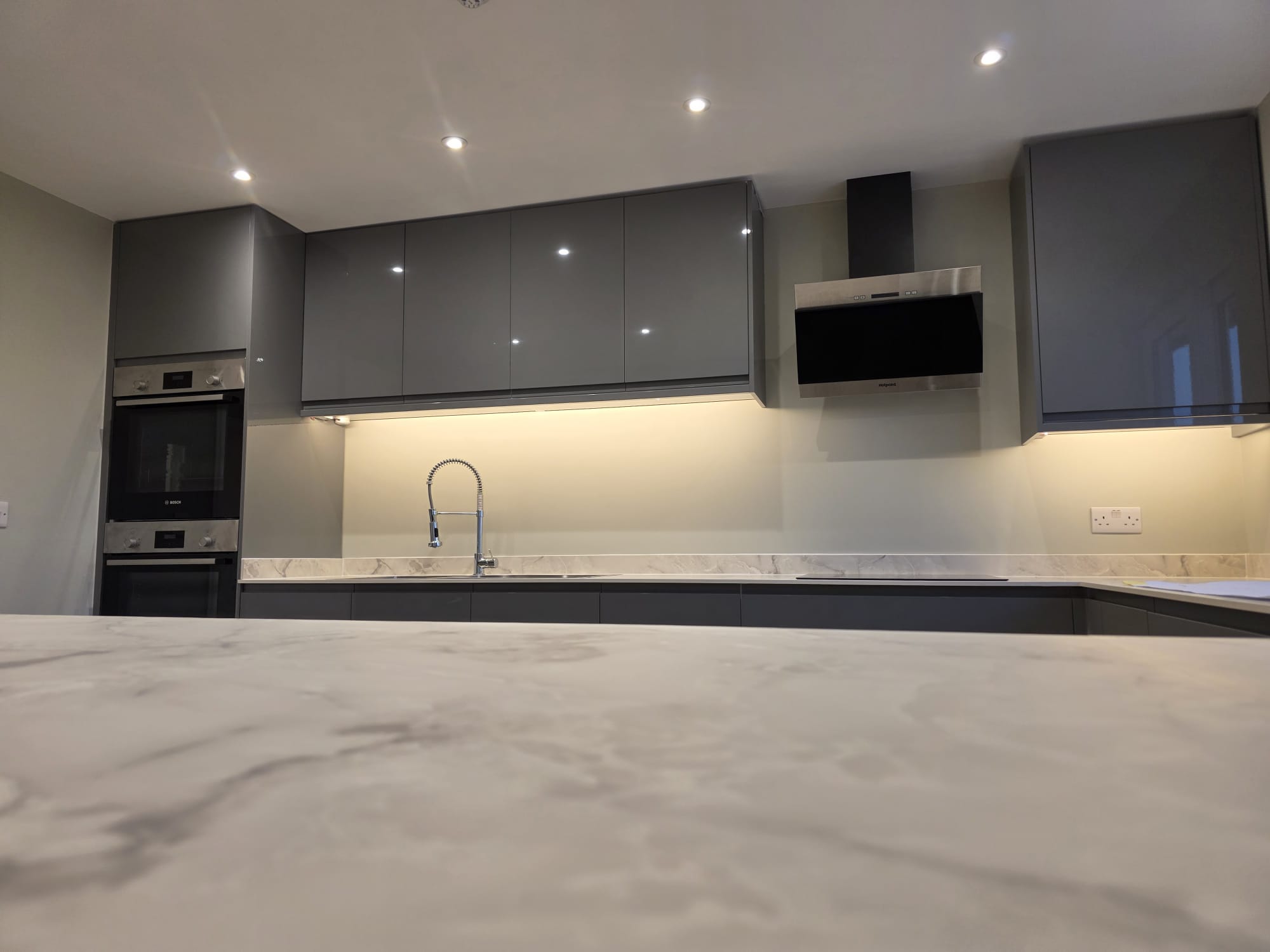 Commercial clubhouse kitchen with grey gloss units, marble effect worktops and extraction, installed by Two Build