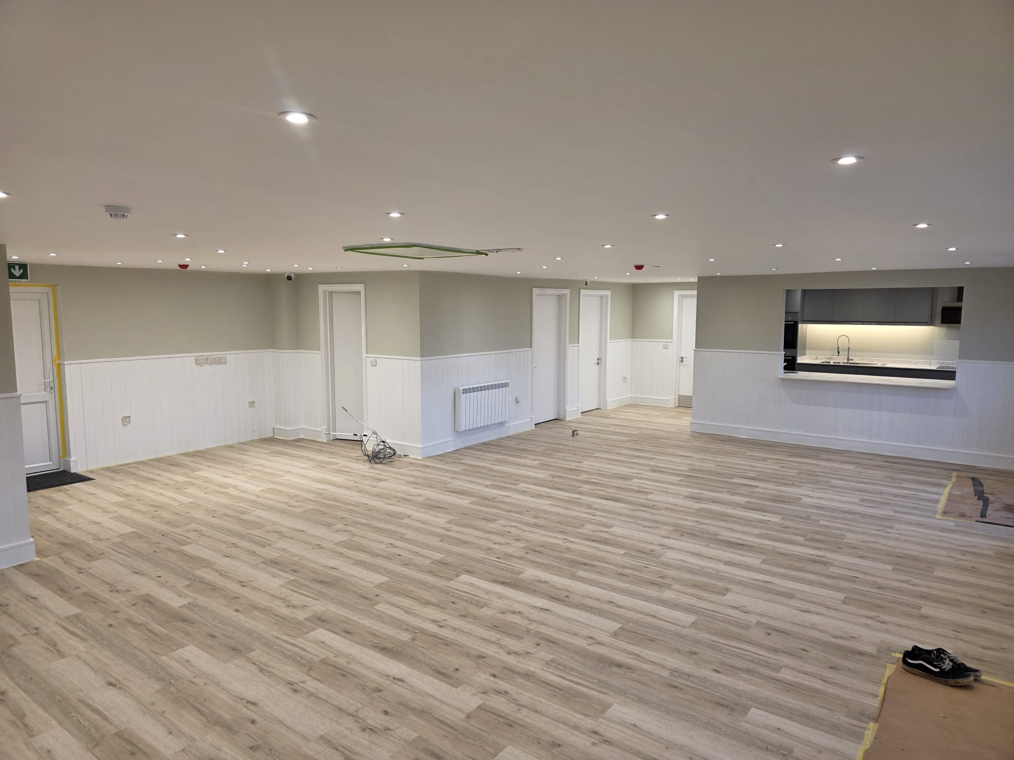 Open plan clubhouse function hall with tongue and groove panelling, luxury vinyl flooring and a servery hatch through to the commercial kitchen